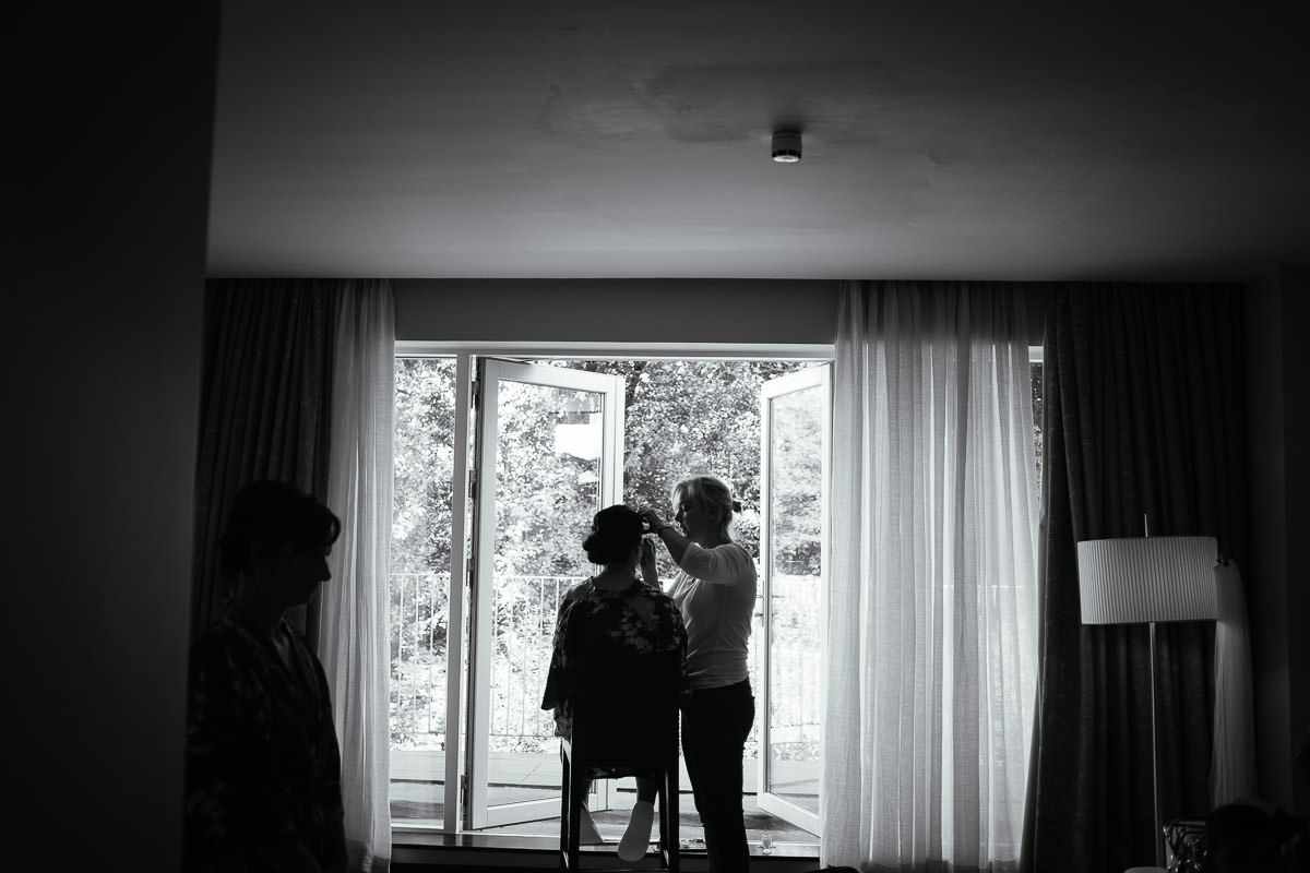 A black and white photo of a bridesmaid having her hair styled by a window at Carton House.