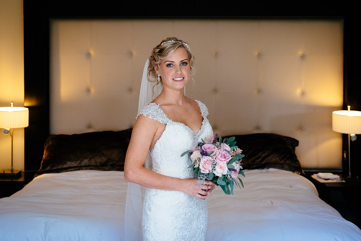 The bride poses with her bouquet in front of the bed at Carton House.