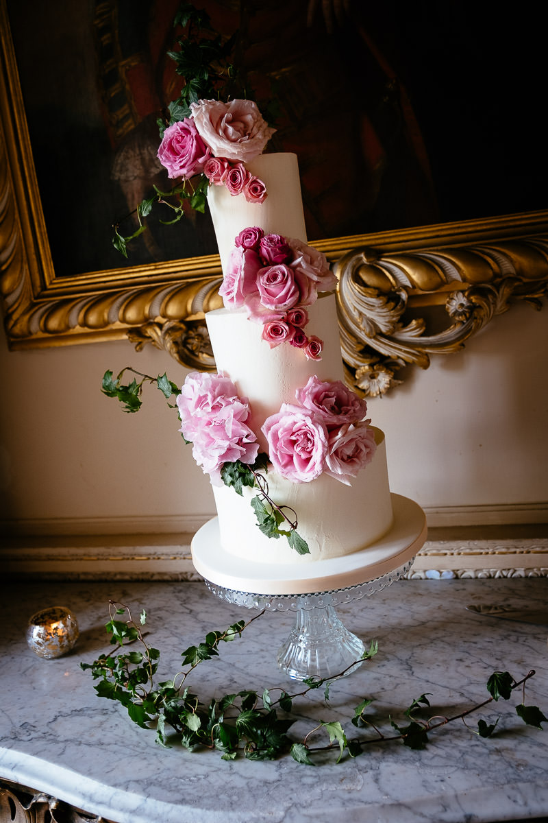 A three-tier wedding cake decorated with pink roses on a marble table at Carton House.