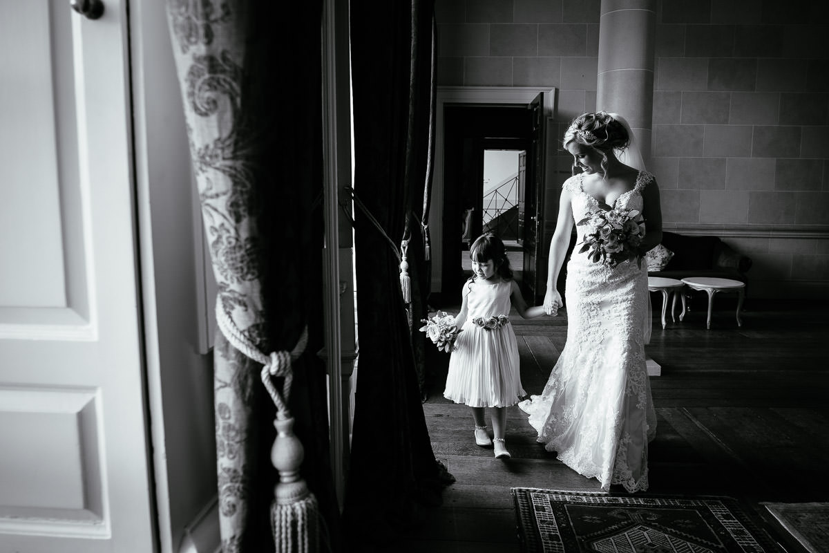The bride holds hands with a flower girl as they walk through the grand hall at Carton House.