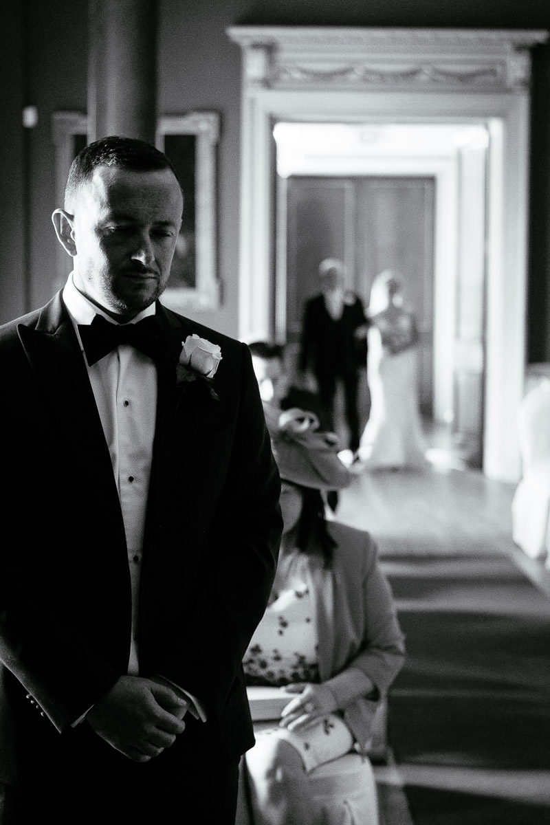 A black and white photo of the groom looking emotional as the bride arrives at Carton House.