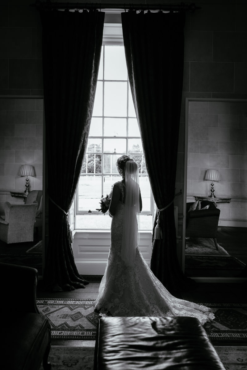 The bride looks out a large window holding her bouquet at Carton House.