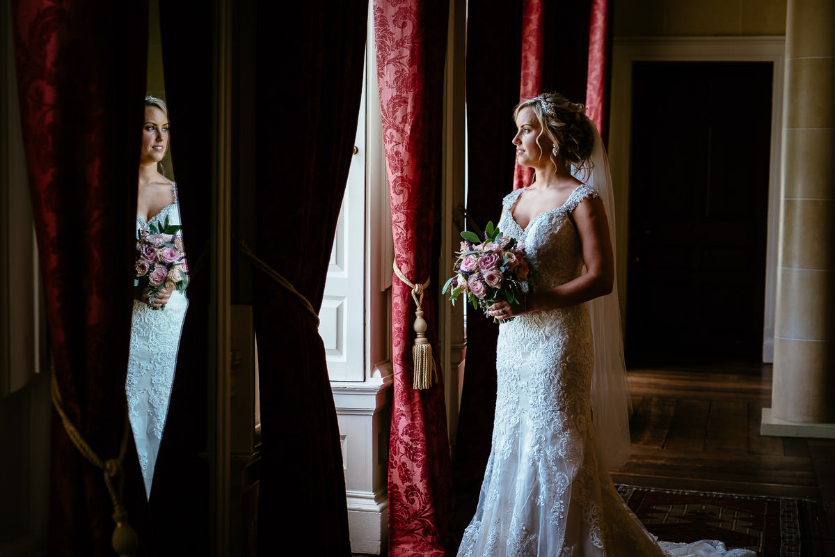 The bride poses beside a mirror reflecting her dress and bouquet at Carton House.