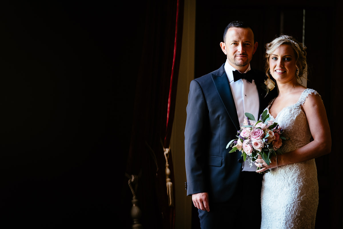 The bride and groom pose together in a dimly lit room at Carton House.