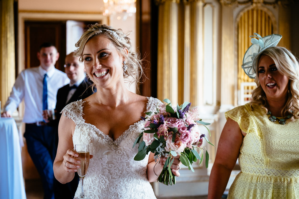 The bride laughs with a glass of champagne while walking with guests at Carton House.