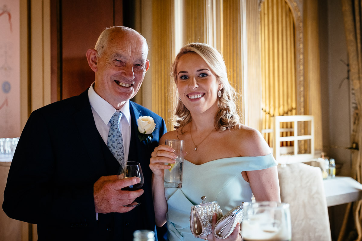 The bride's father poses with a bridesmaid holding drinks during the reception at Carton House.