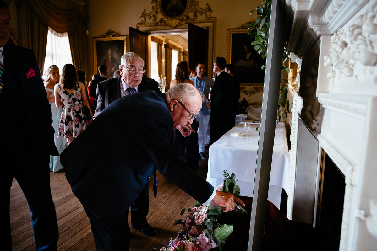 Guests gather around the fireplace as an older man reaches for a bouquet at Carton House.