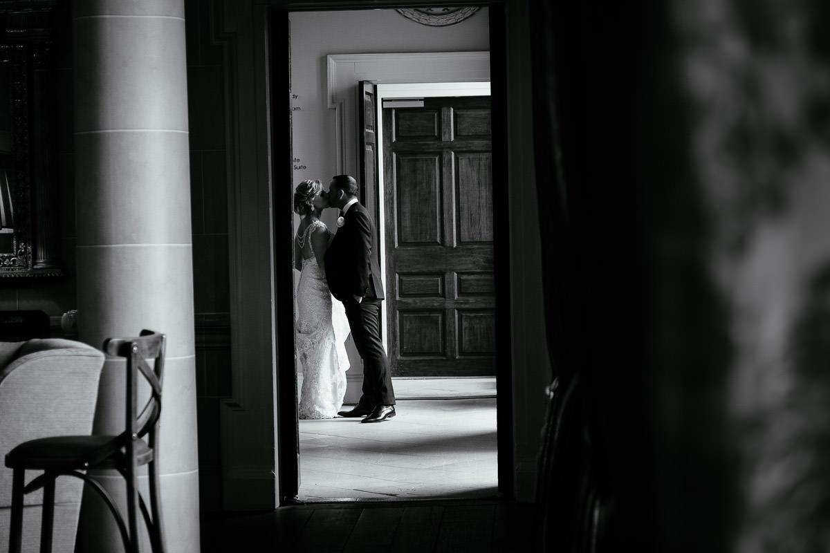 A black and white photo of the bride and groom sharing a kiss in a doorway at Carton House.