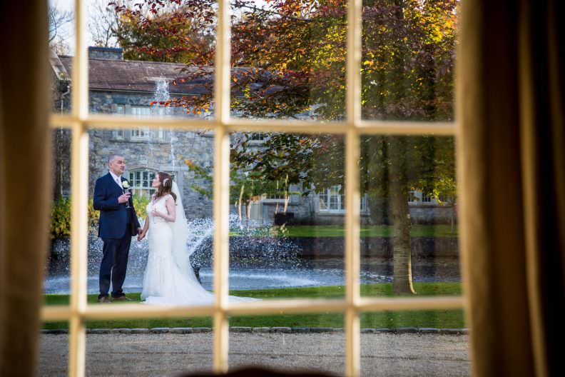 Stunning Wedding at Cliff at Lyons Kildare 10 bride and groom at a water fountain photographed through a window at cliff at lyons, kildare, ireland