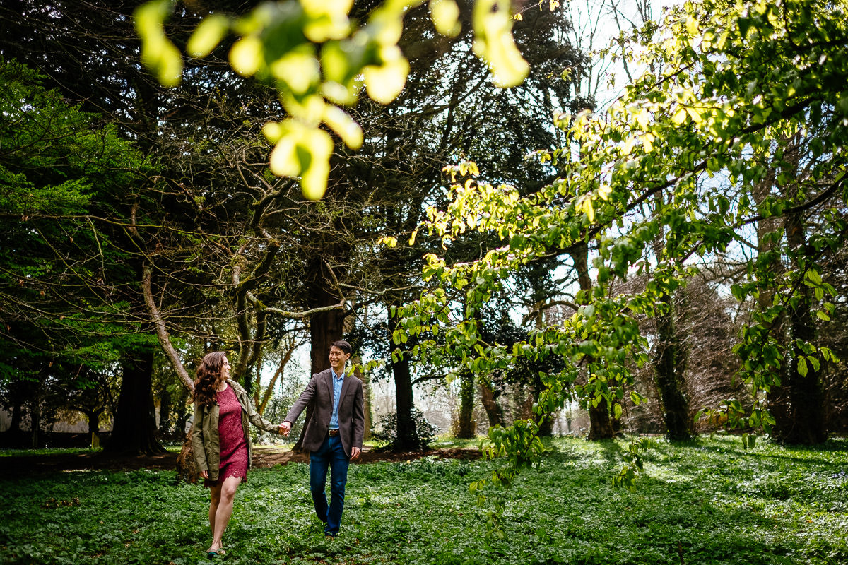 engaged couple walking through filtered sunlight and trees in st annes park