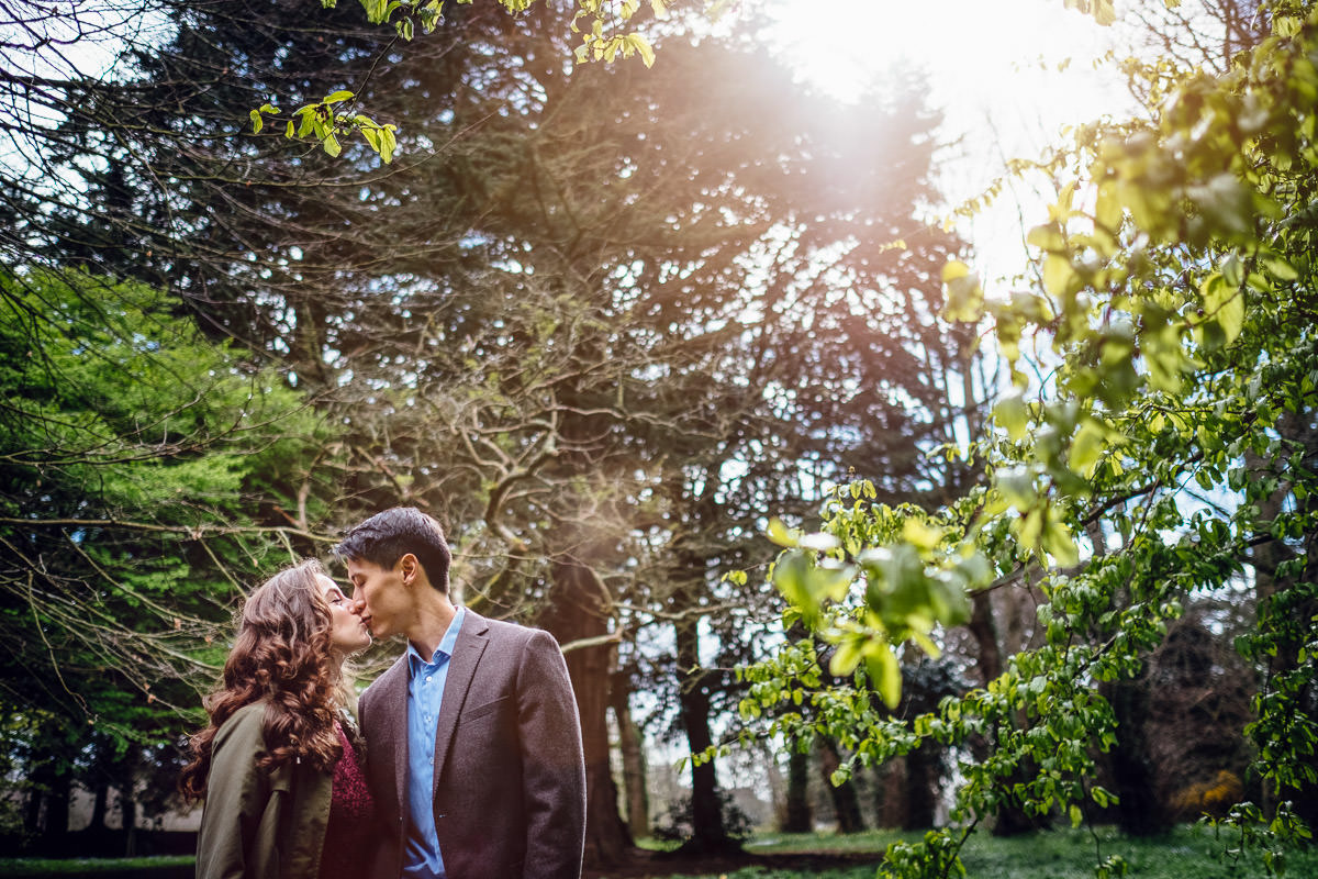 engaged couple kissing through filtered sunlight in st annes park
