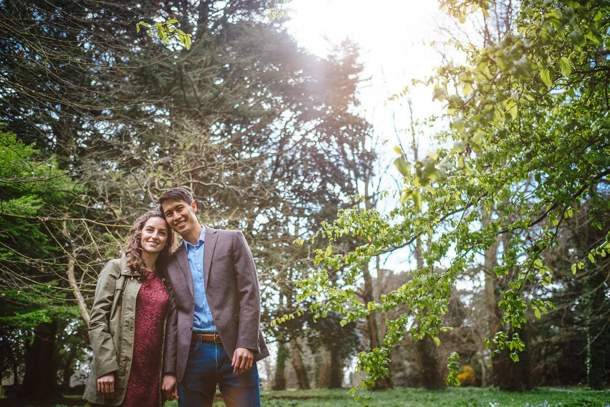 engaged couple posing for caamera through filtered sunlight in st annes park