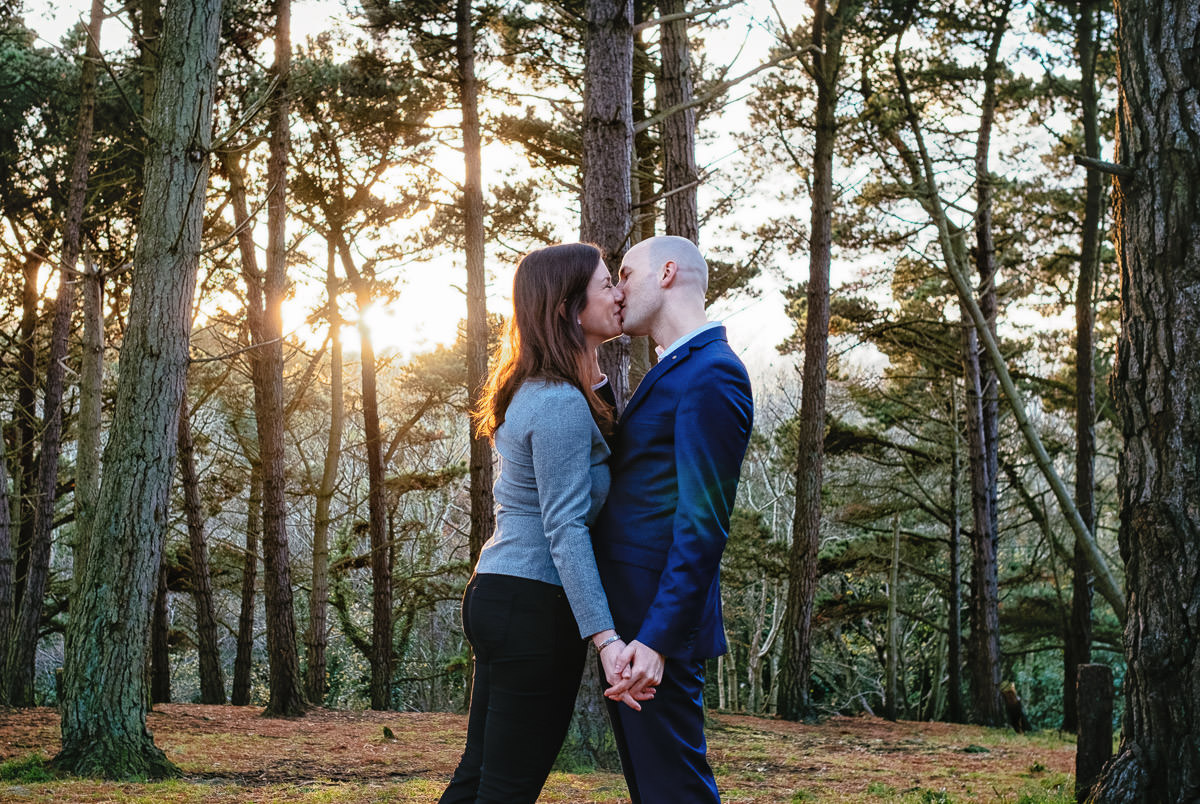 engaged couple kissing in forest at sun set