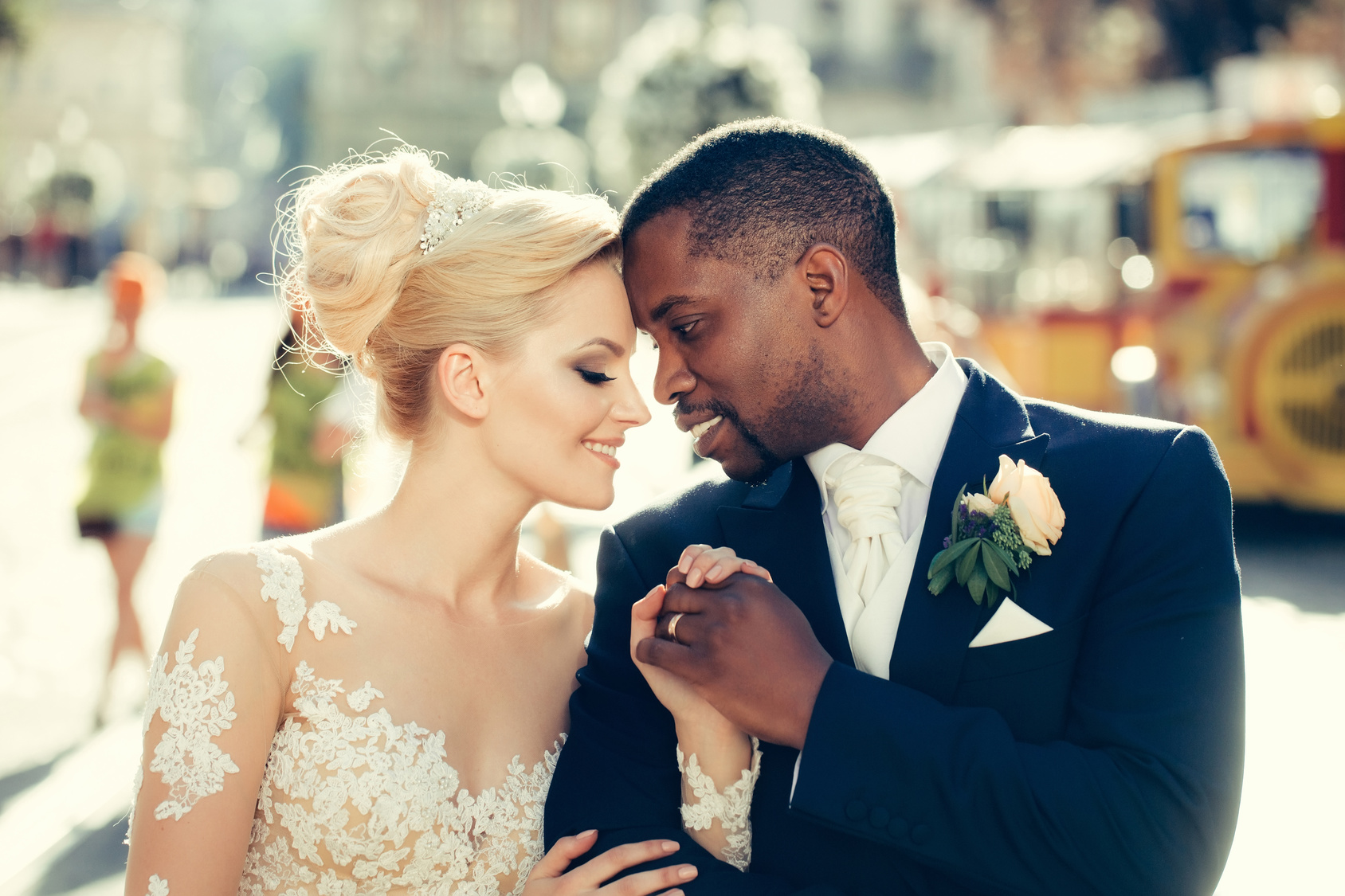 Loving couple of pretty girl or cute bride with beautiful blond hair in white sexy wedding dress and handsome man or african American groom outdoors on sunny day on blurred city street background