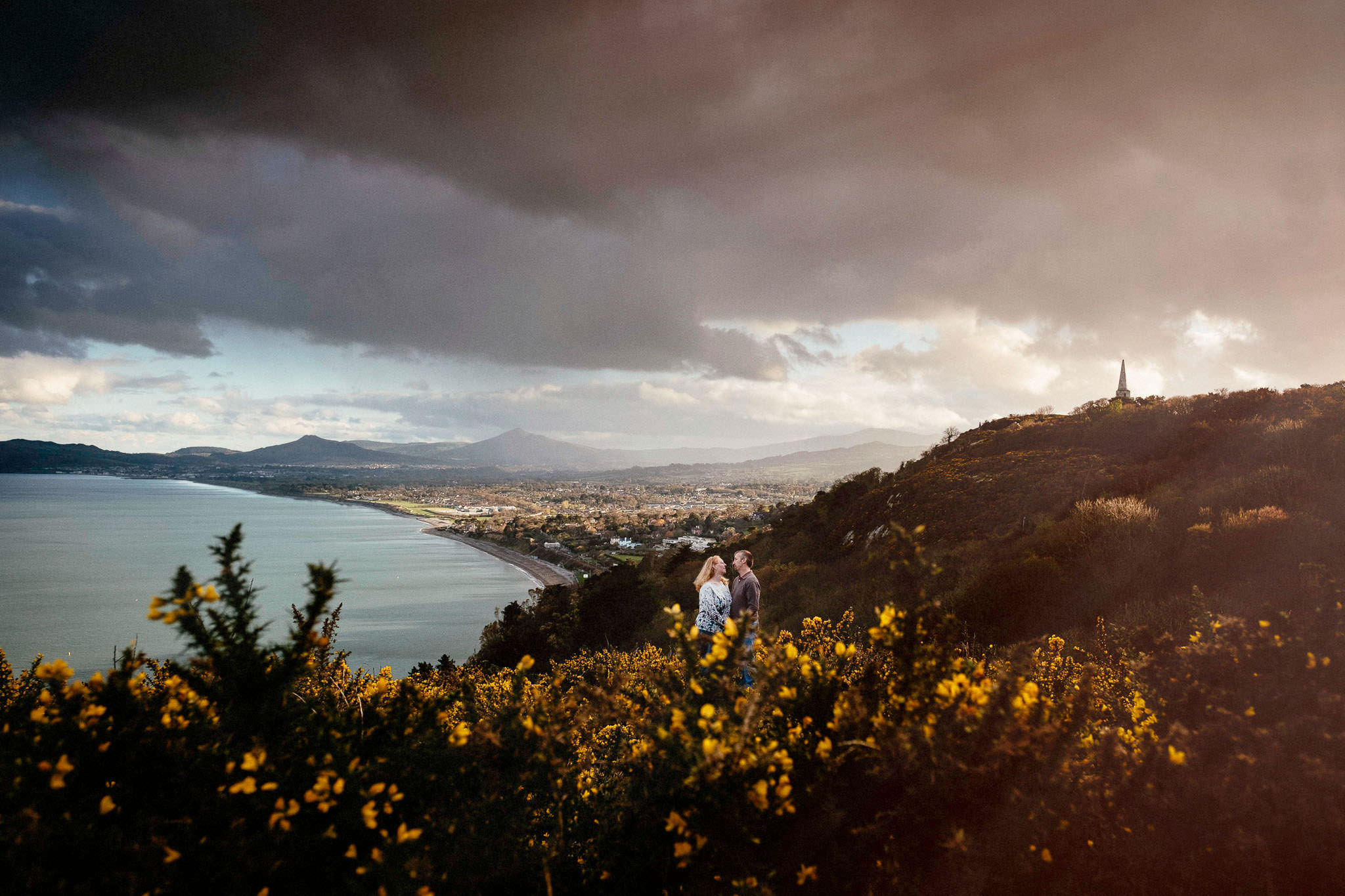 engaged couple making contact on howth head at sunset