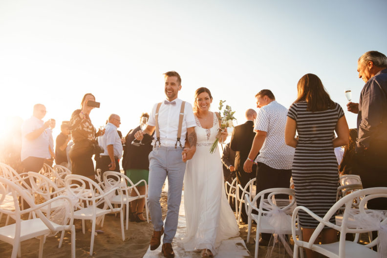 Why a "Perfect" Instagram Feed Doesn't Always Mean a Perfect Wedding Photographer 10 a young good looking bride and groom walking down aisle at their outdoor beach wedding as the sun sets behind them captured by their perfect wedding photographer