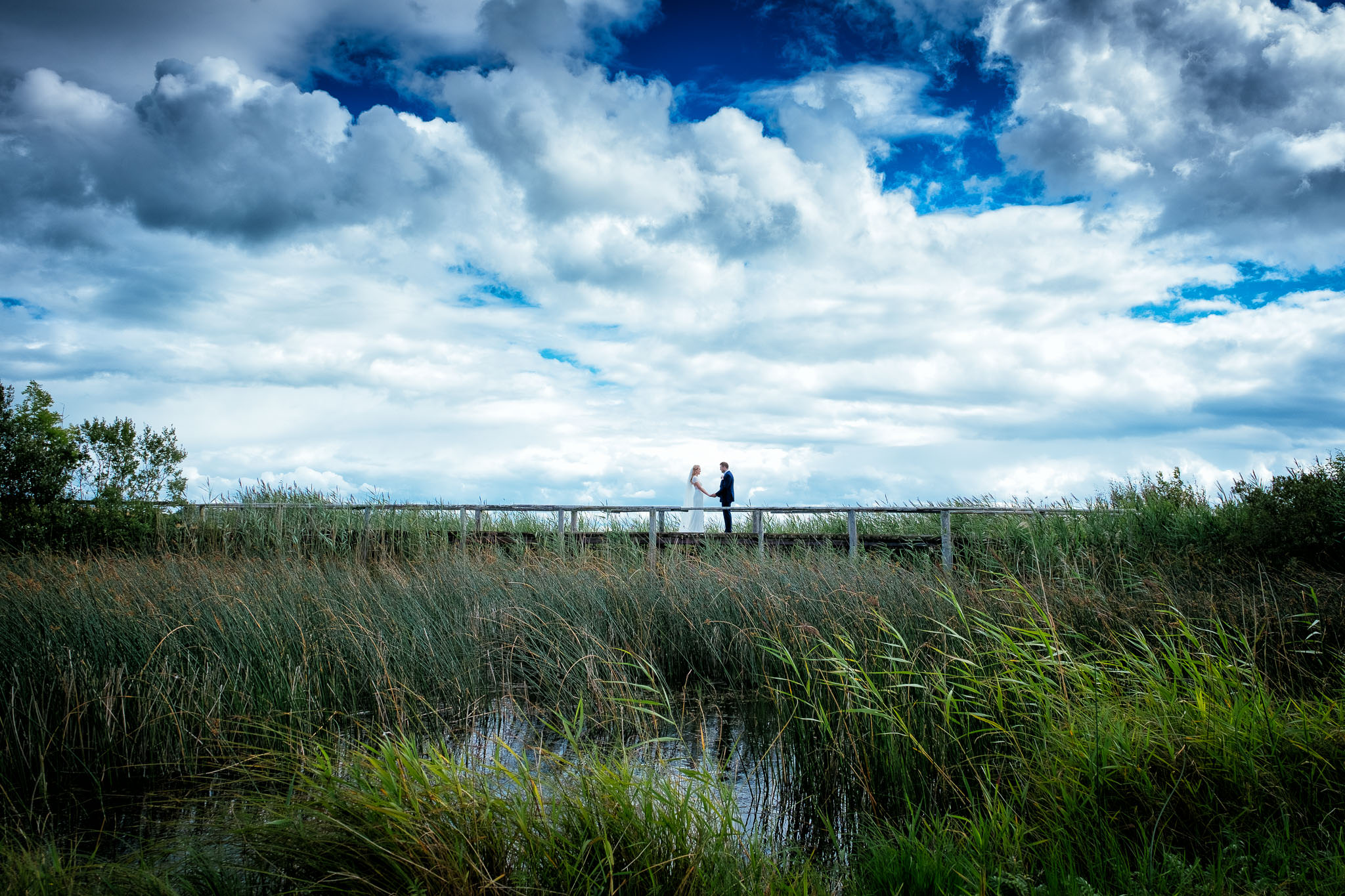 bride and groom standing on a bridge with open sky in the background