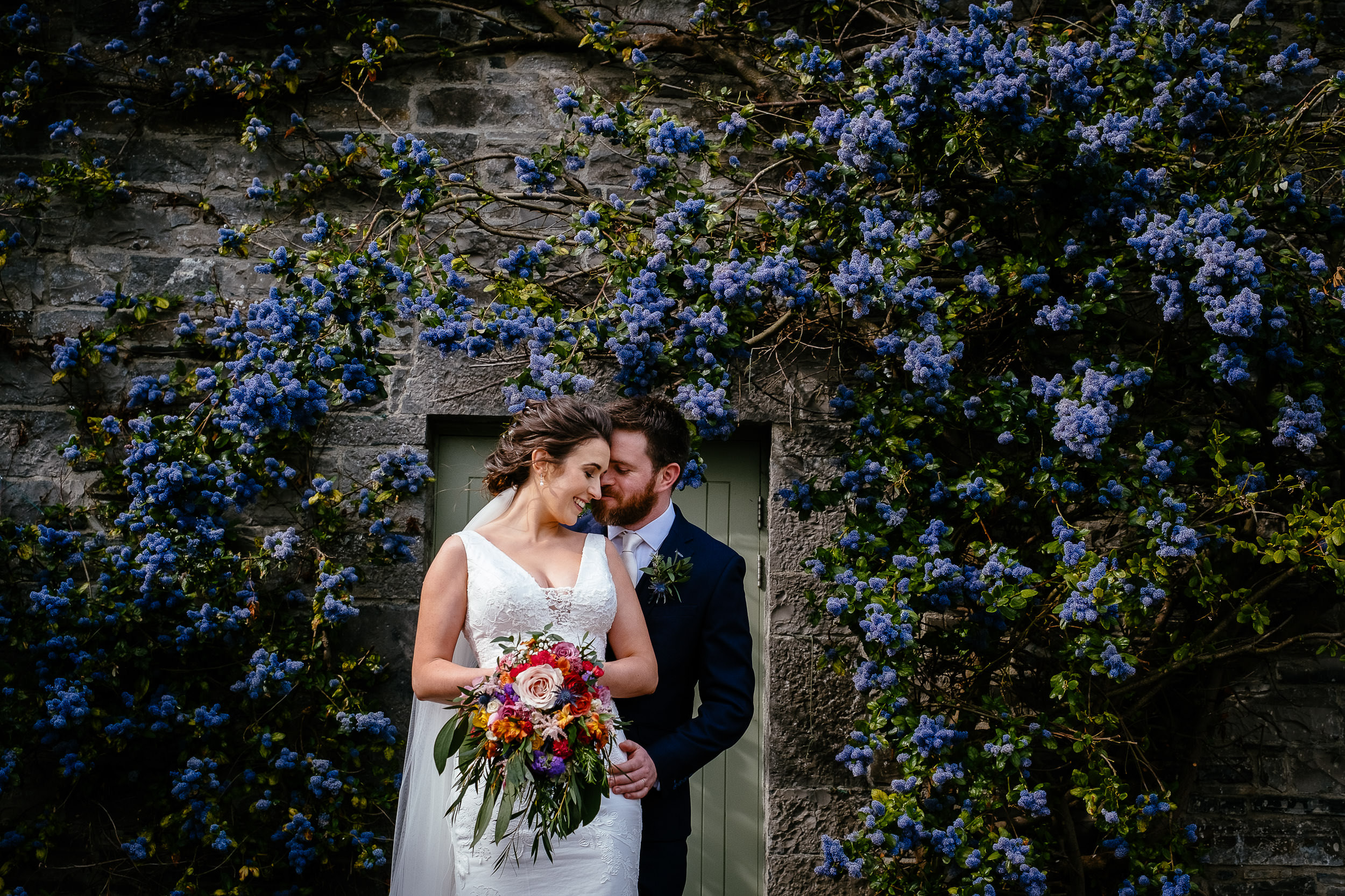 bride and groom embracing in front of doorway with purple flowers at Ballymagarvey village meath