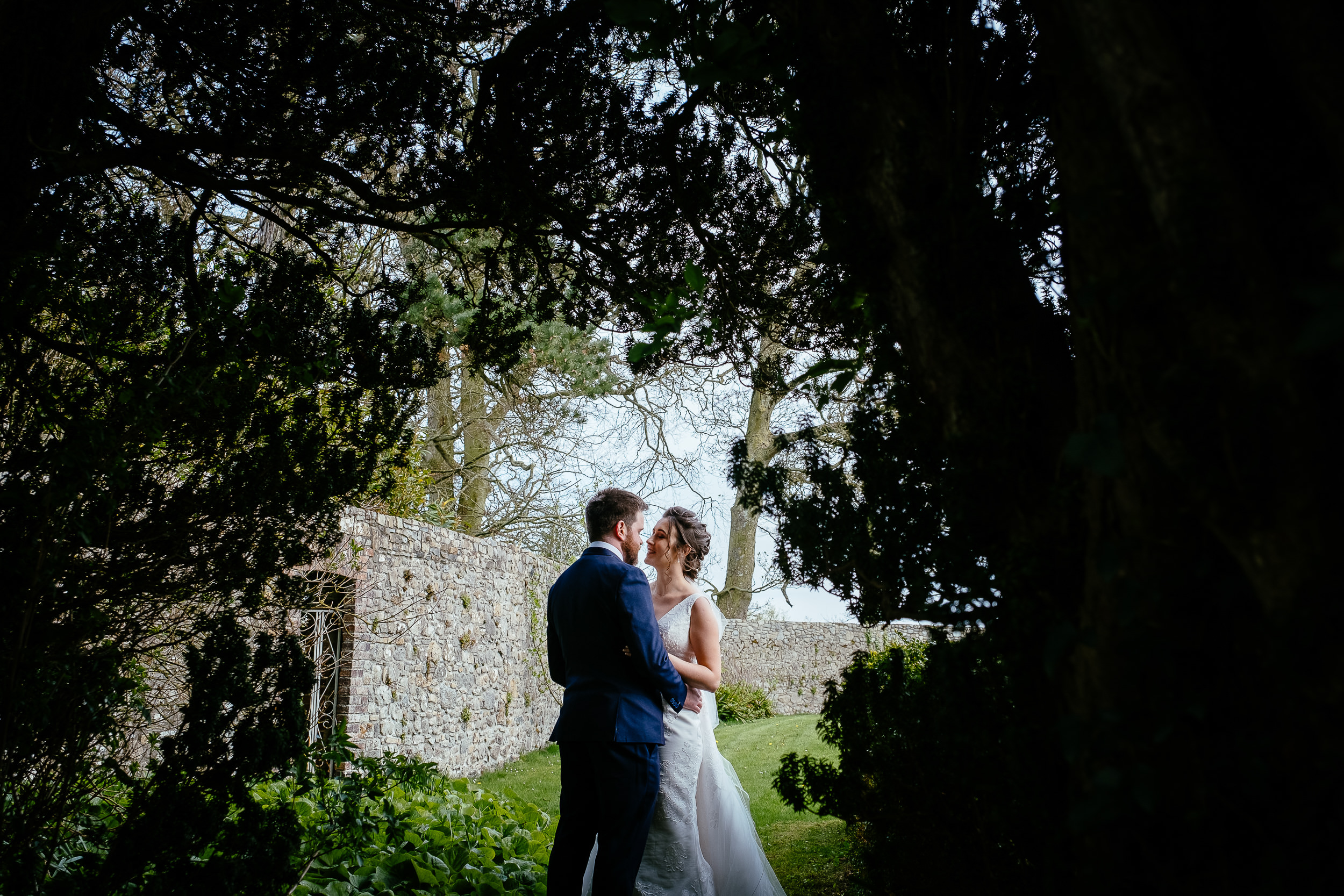 bride and groom kissing through a gap in trees at Ballymagarvey village meath