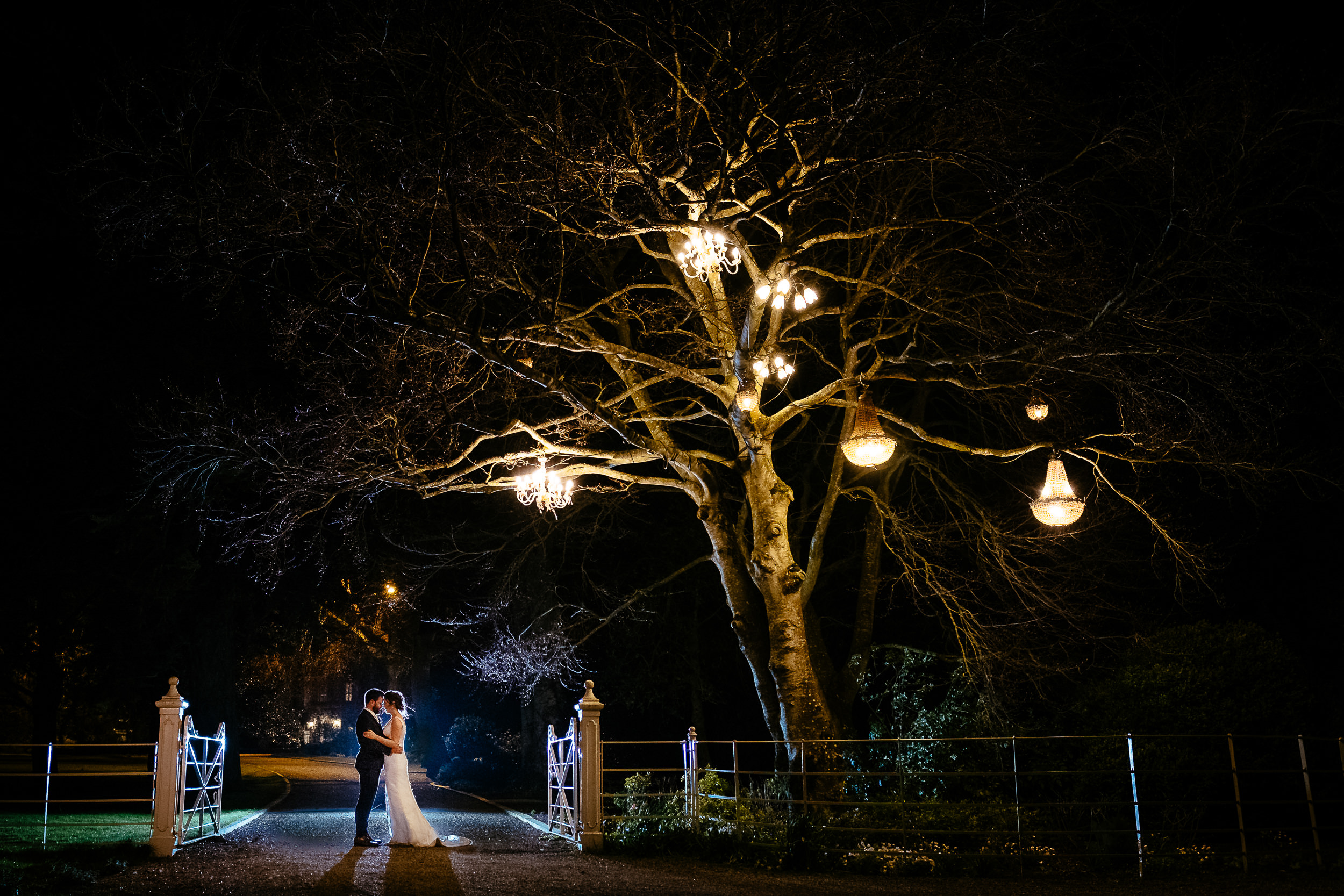 bride and groom embracing under a tree with lanterns at night in ballymagarvey village