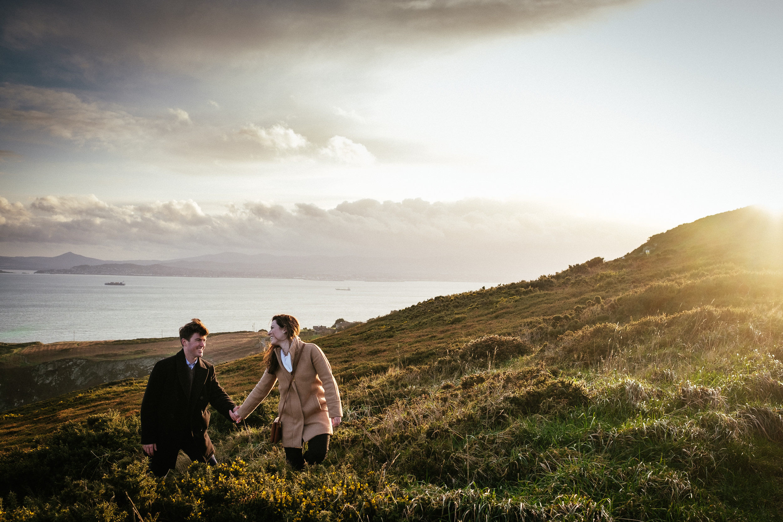 engaged couple walking through heather on the cliff path at howth head dublin