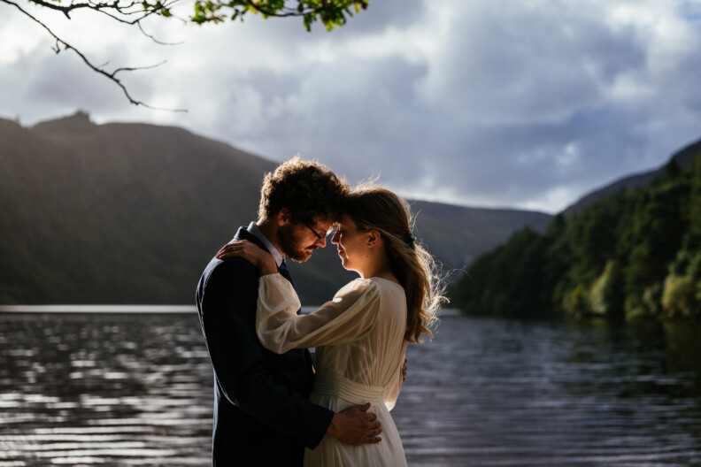 A bride and groom embrace by a lake framed by mountains, showcasing the best location in Ireland for an elopement.