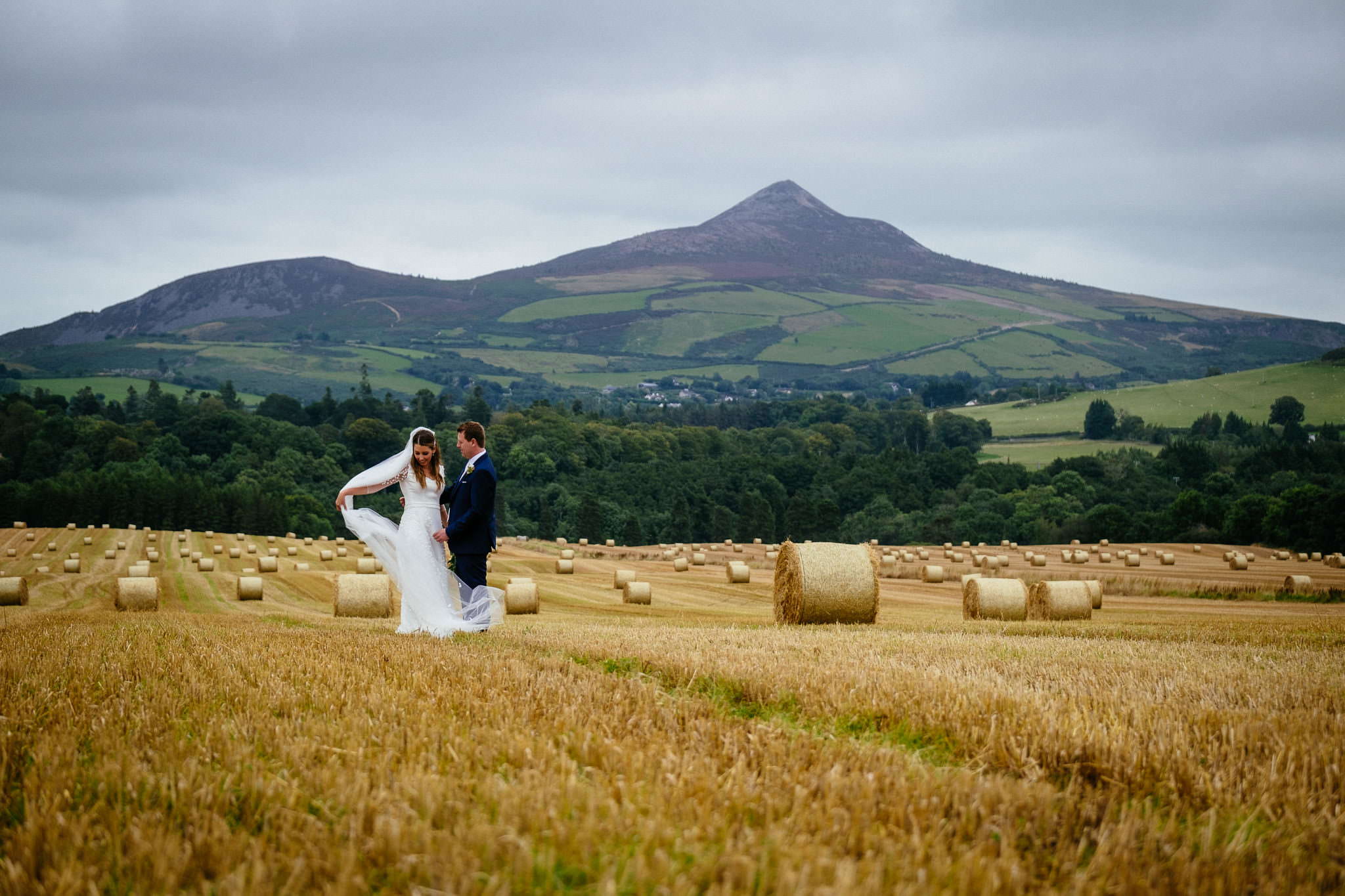 bride and groom standing in a field with the Sugarloaf mountain in the background after their Wedding at the 5 Star Powerscourt Distillery Wicklow Ireland