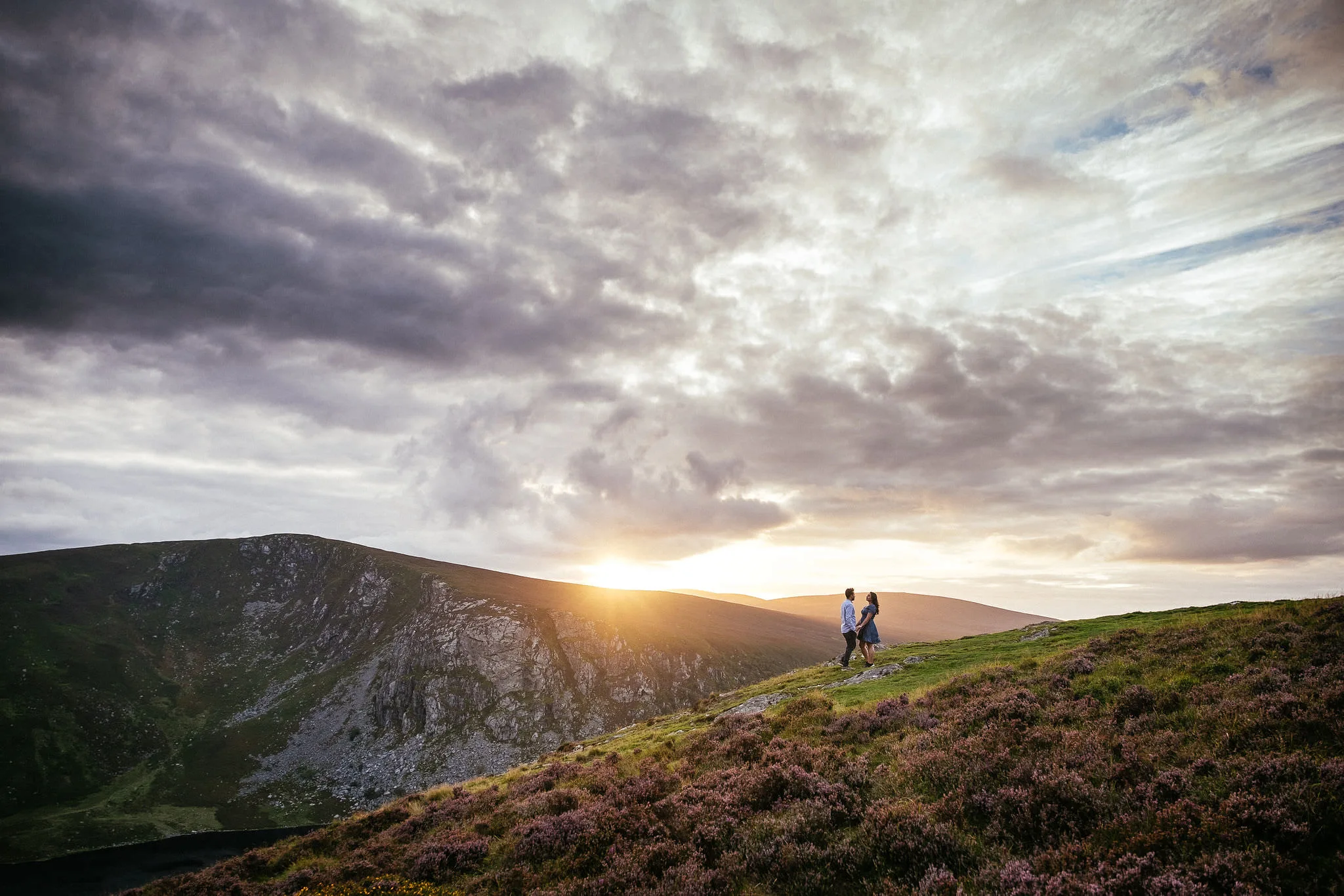 A couple walking a hillside at sunset with mountains behind, Ireland