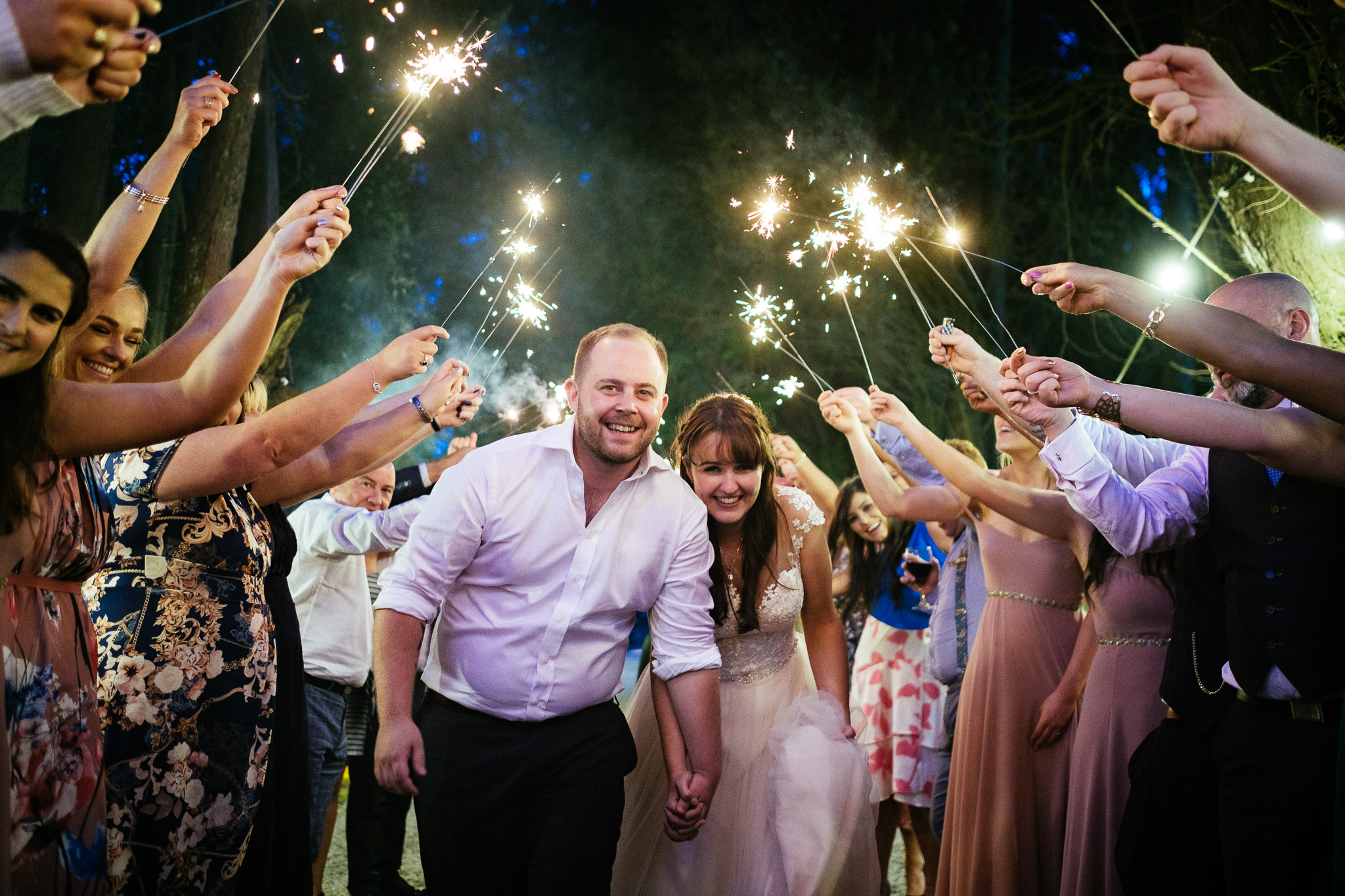 A bride and groom walk through a tunnel of sparklers held by cheering guests at Ballybeg House Wicklow - Wedding Photographer in Ireland