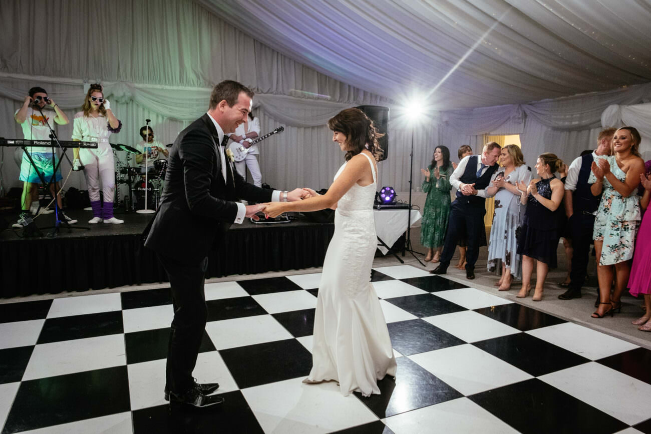A bride and groom gracefully dancing on a black and white checkered dance floor during their elegant wedding at Trump International Hotel Doonbeg.