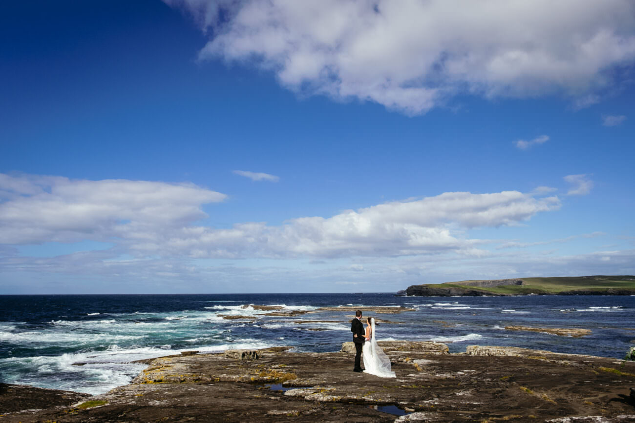 A bride and groom having their wedding ceremony at Trump International Hotel Doonbeg, standing on a rocky cliff overlooking the ocean.