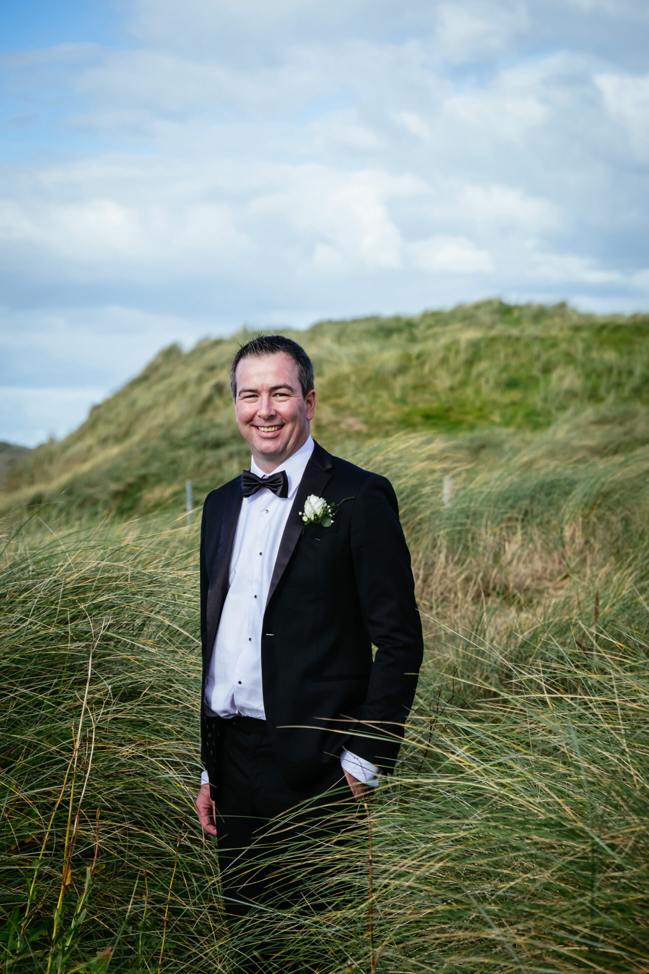 A man in a tuxedo standing in tall grass at a glamorous wedding held at Trump International Hotel Doonbeg.