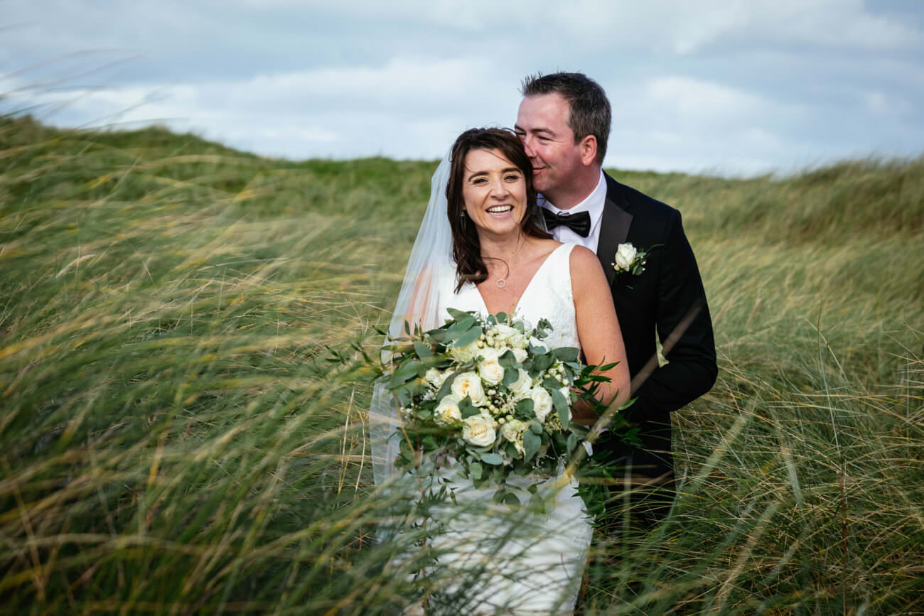 A wedding party at Trump International Hotel Doonbeg, with the bride and groom standing in tall grass.