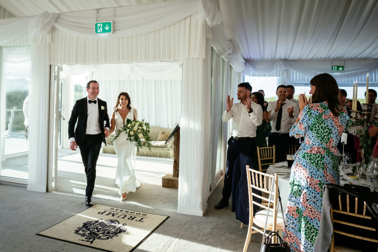 A bride and groom, celebrating their wedding at Trump International Hotel, Doonbeg, joyfully walk out of a tent.