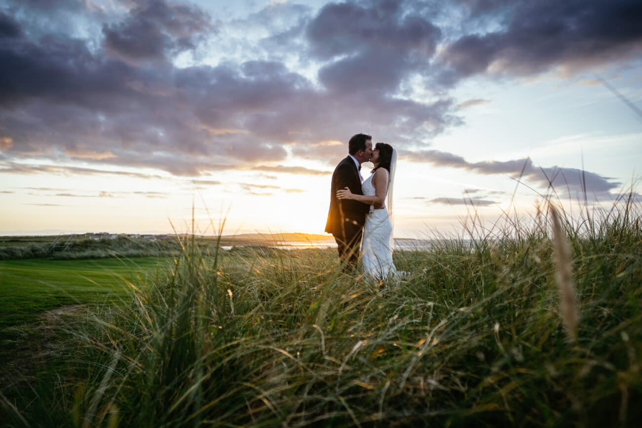 A bride and groom sharing their first kiss in tall grass at sunset during their wedding at Trump International Hotel Doonbeg.