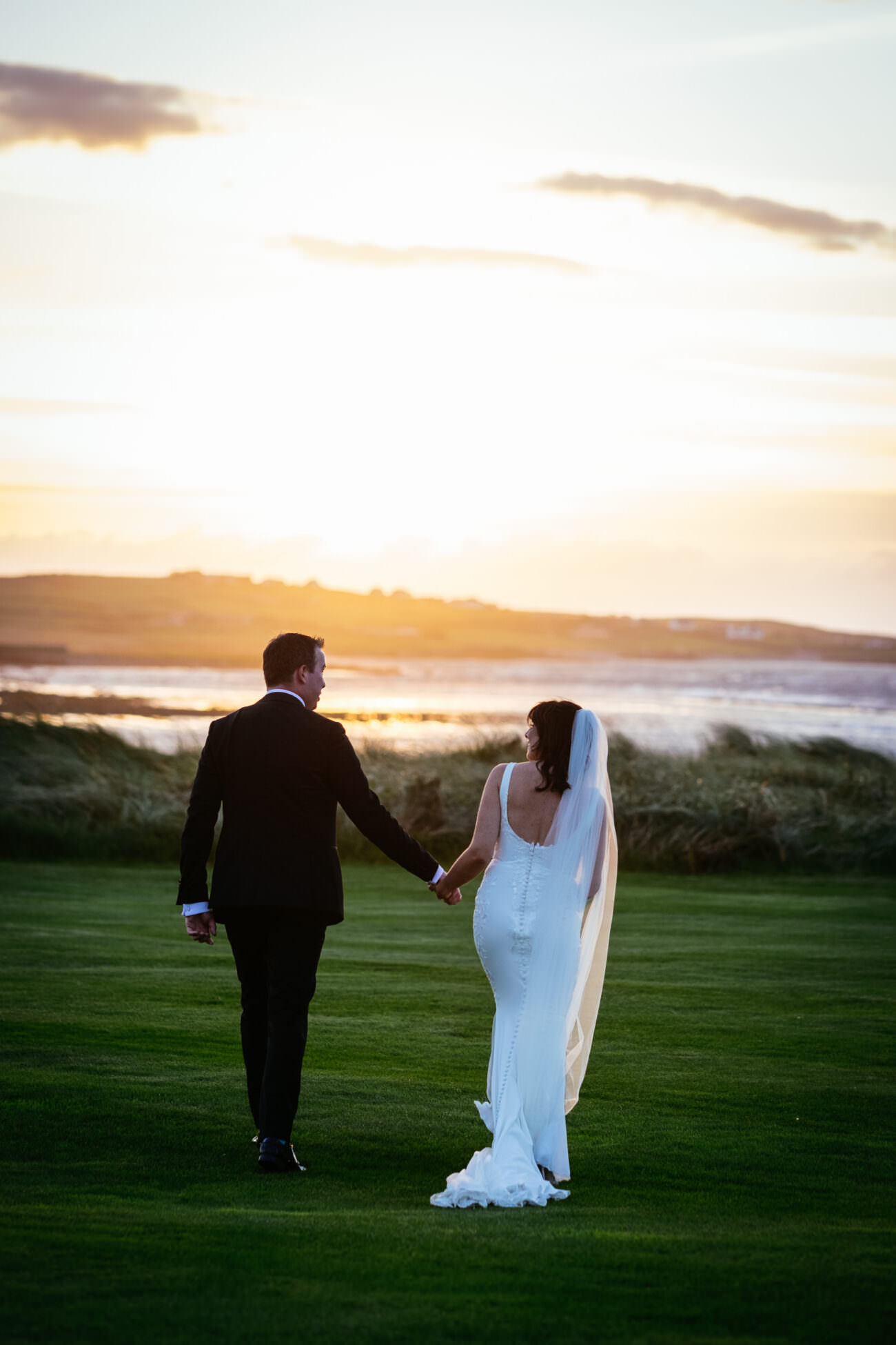 A bride and groom enjoying a romantic stroll on a grassy field at sunset at their wedding at Trump International Hotel Doonbeg.