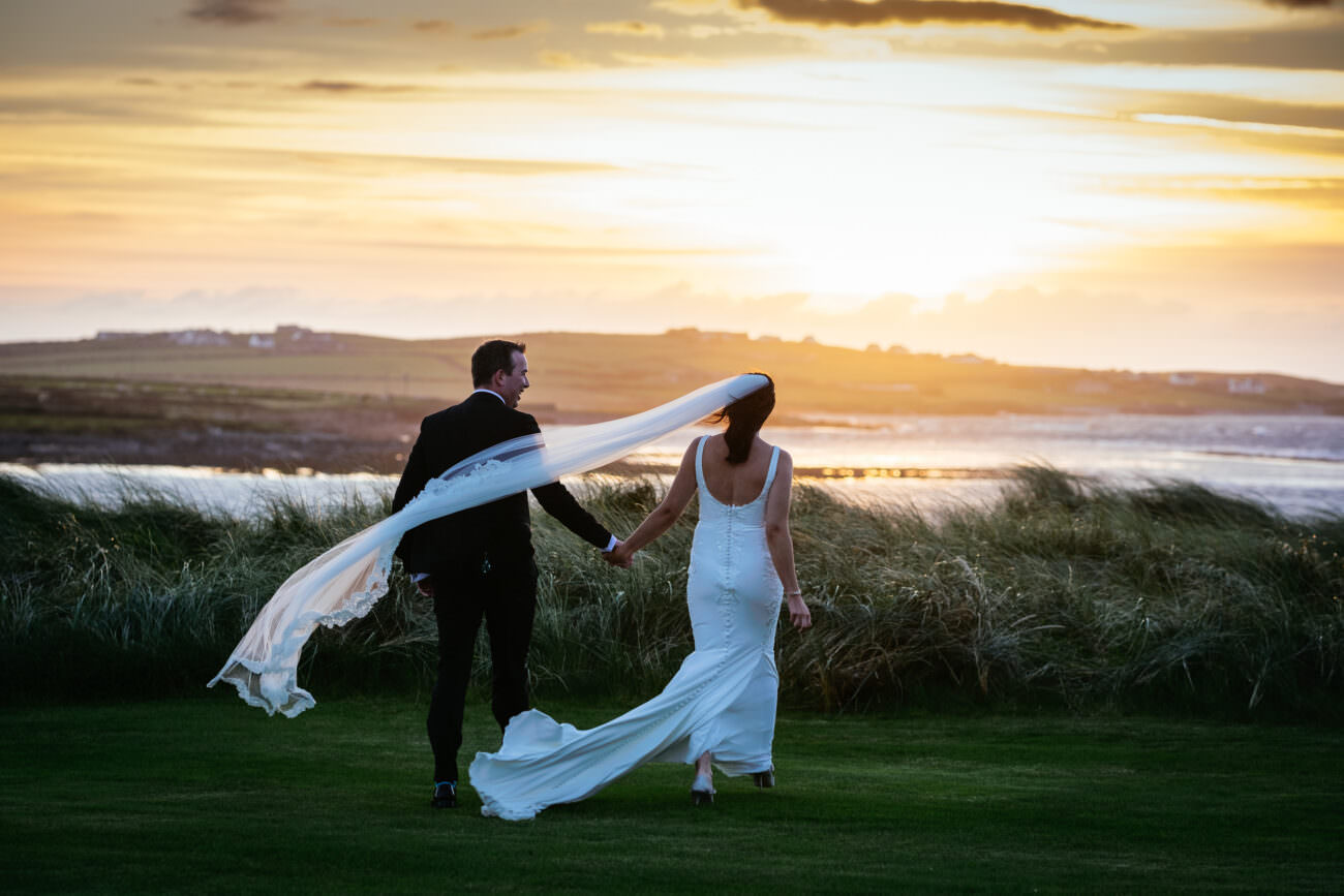 A bride and groom walking down a grassy field at sunset during their wedding at Trump International Hotel Doonbeg.