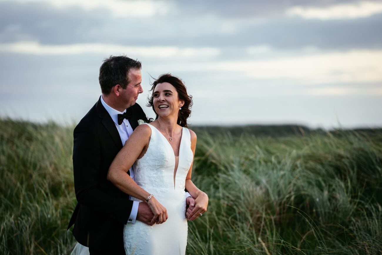 A bride and groom standing in a field at sunset, capturing the romantic ambiance of their wedding at Trump International Hotel Doonbeg.