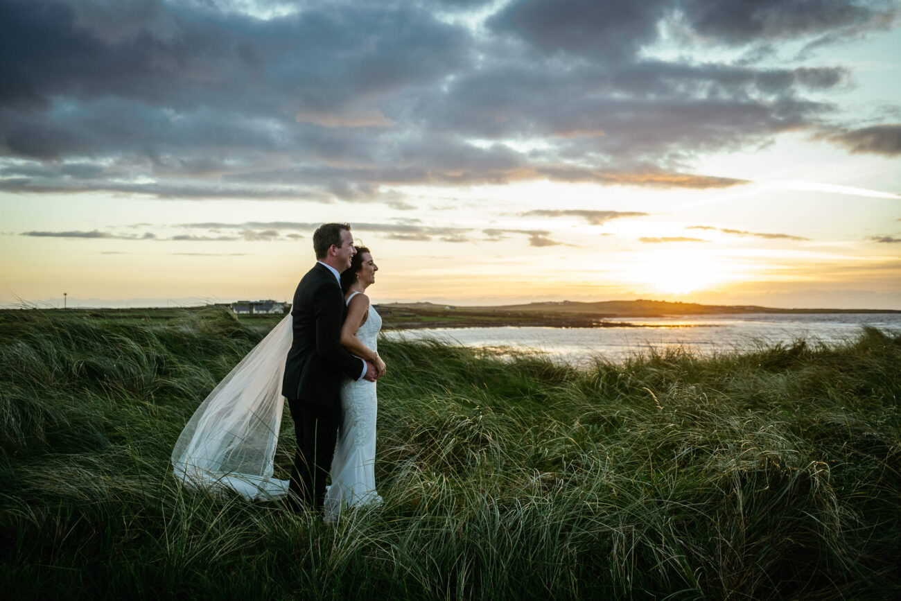 A bride and groom standing in the grass at sunset during their Wedding at Trump International Hotel Doonbeg.
