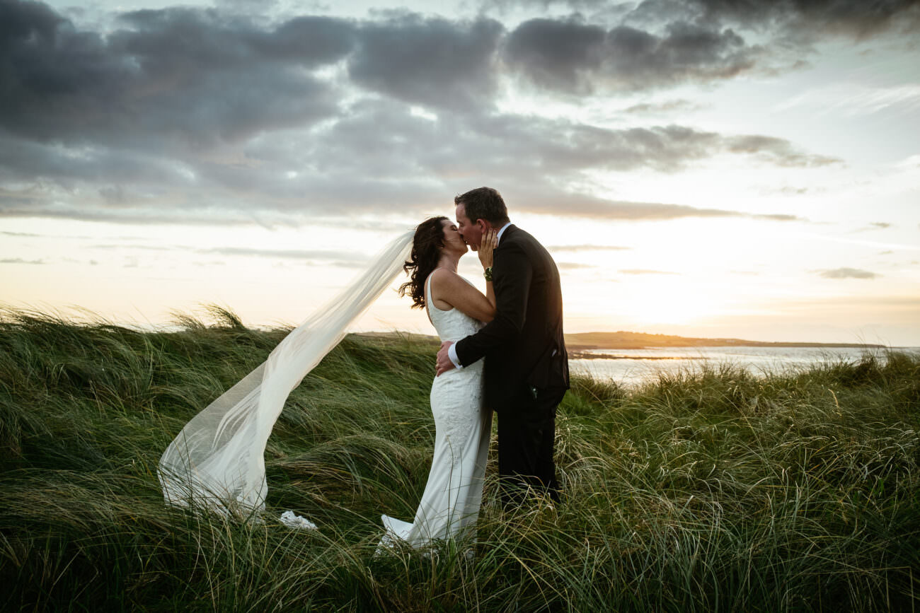 A bride and groom kissing at Trump International Hotel Doonbeg during a sunset wedding ceremony on the grass.