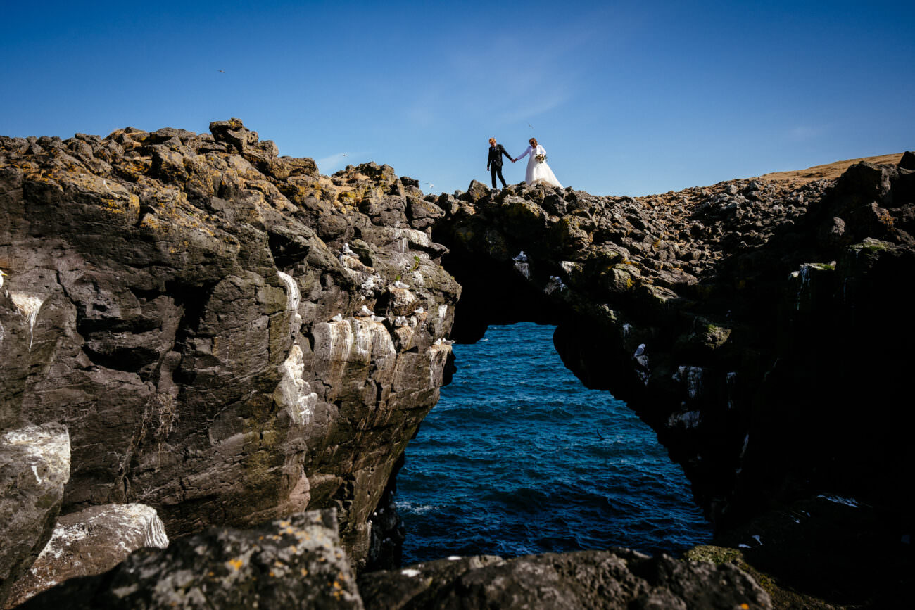 bride & groom walking by a sea arch on the Snæfellsnes Peninsula during her elopement