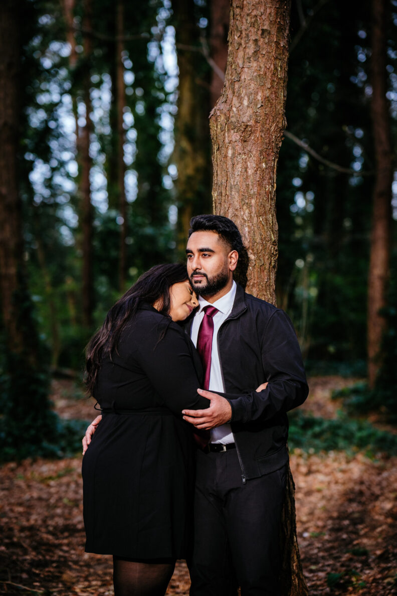 A man and woman hugging in the woods.