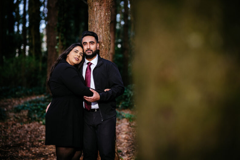A man and woman hugging in the woods.