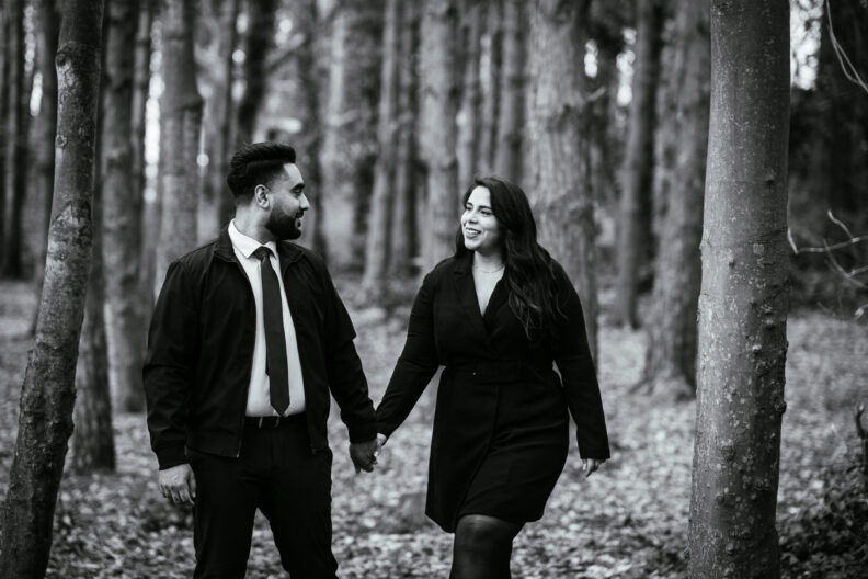 A black and white photo of an engaged couple walking through the woods.