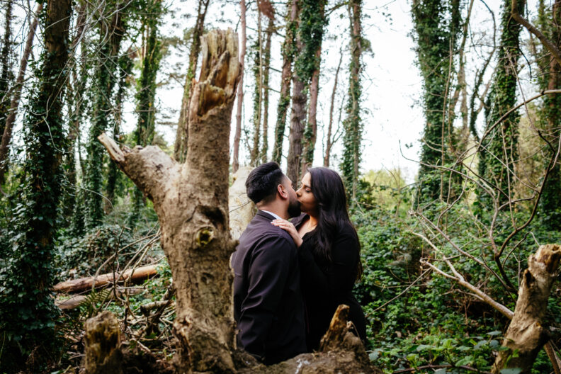 An engaged couple kissing in the woods.