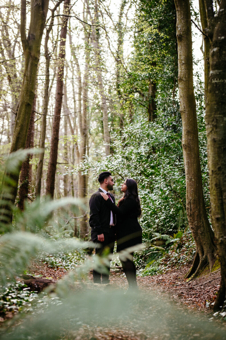 An engaged couple standing in a wooded area.