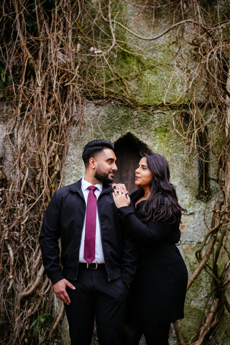 An engaged couple posing in front of a stone wall.