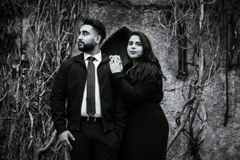 A black and white photo of a couple posing in front of a stone wall.
