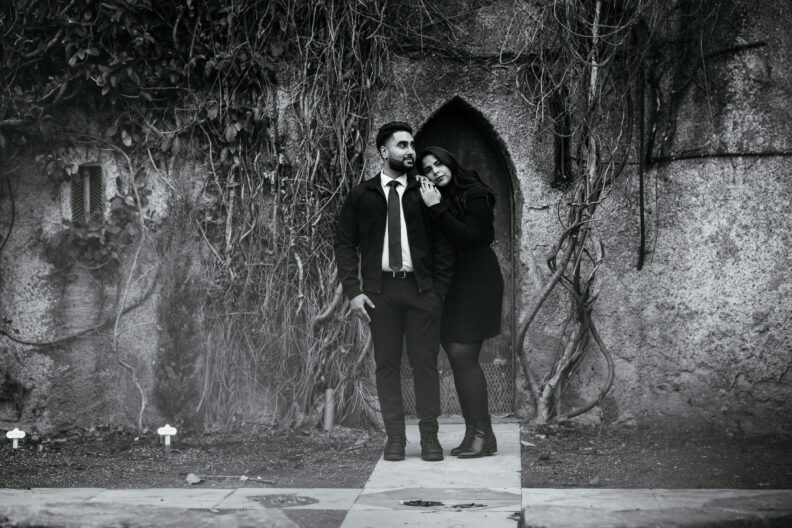 A black and white photo of a couple posing in front of an old building.