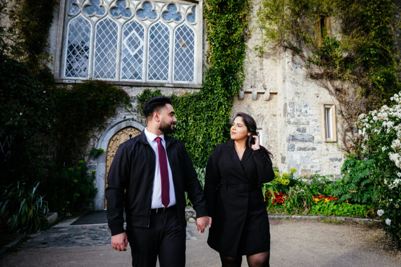 An engaged couple holding hands in front of a castle.